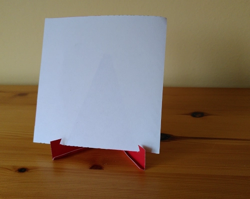 a small DIY stand made from red cardboard with a a small sheet of notepad paper on it