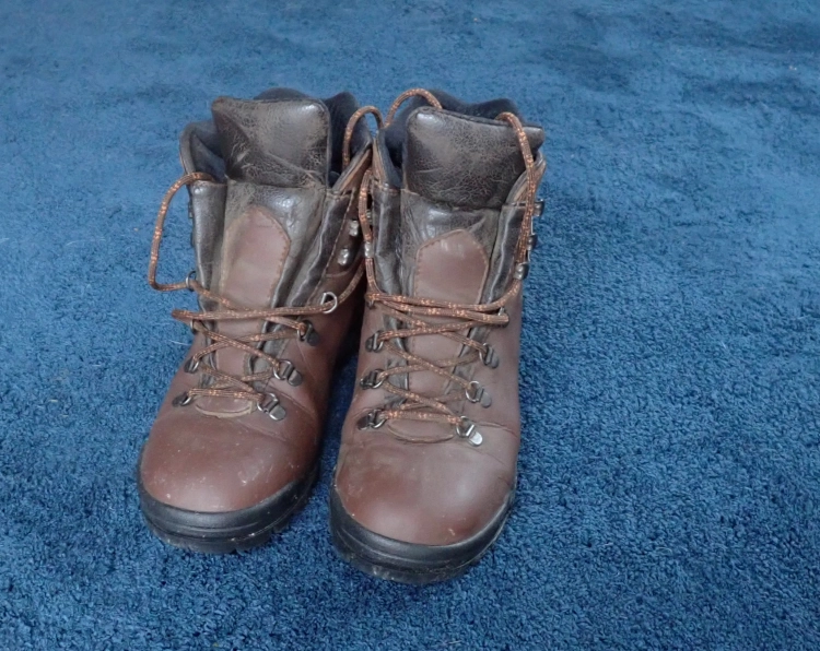 A pair of well worn browm boots on a blue carpet