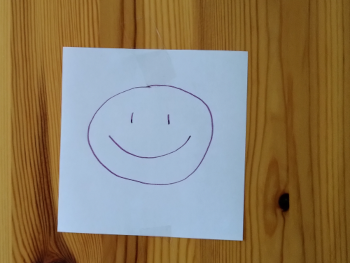 über mich: Photo von einem Notizzettel, auf dem ein Smiley aufgemalt ist