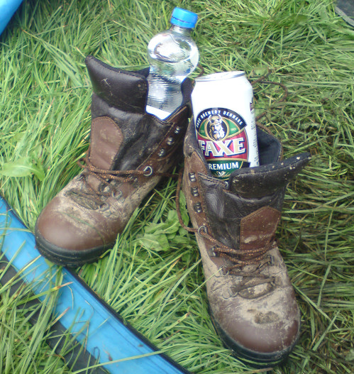 ein paar Stiefel im Gras im Eingangsbereich eines Zeltes. Im einen Stiefel steckt eine Flasche Wasser, im anderen eine Faxedose