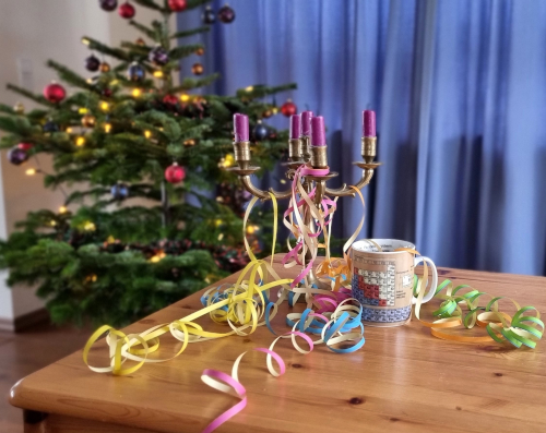 Neujahr: Ein Weihnachtsbaum im Hintergrund, vorne ein Tisch, darauf Luftschlangen und ein leeres Sektglas.