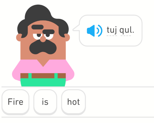 Screenshot aus der App Duolingo. Ein Cartoonmann mit Schnurrbart sagt in einer Comicblase einen Satz auf Klingonisch. Darunter steht die englische Übersetzung: "Fire is hot"