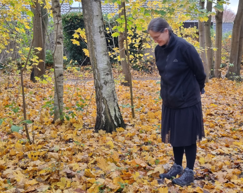 Eine Frau steht im Wald auf goldenem Herbstlaub und schaut auf den Boden.