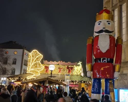 Blick auf einen abendlichen Weihnachtsmarkt VOrne rechts im Bild ist eine meterhohe Nussknackerfigut