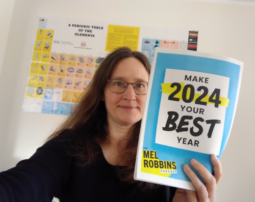 Eine Frau hält ein Workbook hoch, auf dem bunten Cover steht Make 2024 your best year