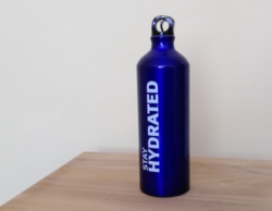 Eine blaue Stahltrinkflasche auf einem Holztisch. Auf der Flasche steht in weiß "stay hydrated"