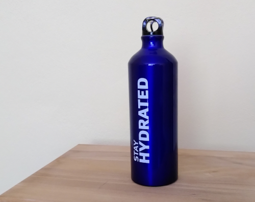 Eine blaue Stahltrinkflasche auf einem Holztisch. Auf der Flasche steht in weiß "stay hydrated"