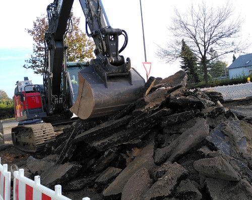 Ein Bagger hinter einem Haufen Asphaltbrocken