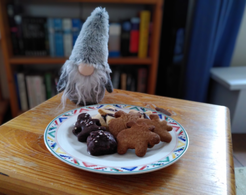 12 von 12 dezember 24: Photo von einem Teller mit Weihnachtskeksen auf einem Beistelltisch. Neben dem Teller steht ein Plüschwichtel mit langem weißem Bart und einer hohen grauen Zipfelmütze