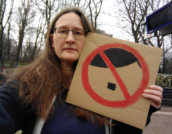 Selfie von einer Frau mit einem Demoschild. Darauf ein Verbotsschild, bestehend aus einem roten Ring und einem roten Streifen schräg darüber. In dem Verbotsschils ist eine Seitenscheitelfrisur und ein kleiner Schnurrbart angedeutet.