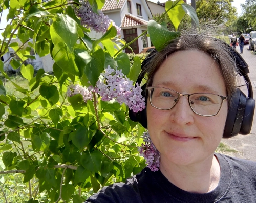 Selfie einer Frau, die ihren Kopf lächend in die Krone eines blühenden Fliederbaumes lehnt