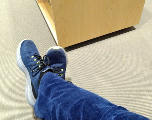 Zwei Beine in einer flauschigen blauen Hose mit blauen Turnschuhen auf einem hellen Fußboden.