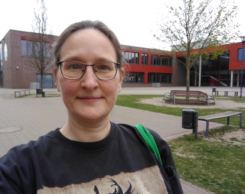 Selfie von einer lächelnden Frau vor einem Schulgebäude