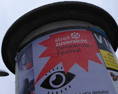Litfaßsäule, daran hängt ein Plakat mit der Aufschrift: Streit, Zuversicht, Demokratiefestival