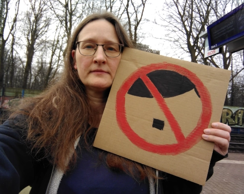 Selfie von einer Frau mit einem Demoschild. Darauf ein Verbotsschild, bestehend aus einem roten Ring und einem roten Streifen schräg darüber. In dem Verbotsschils ist eine Seitenscheitelfrisur und ein kleiner Schnurrbart angedeutet.