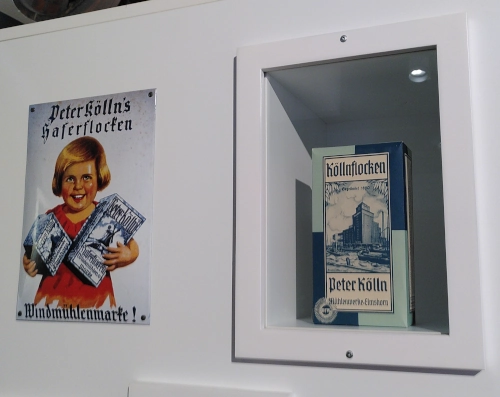 Eine Vitrine, in der eine historische Köllnflockenpackung steht, daneben ein werbeschild für Köllnflocken mit einem fröhlichen Kind