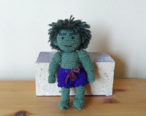 Photo von einer Häkelfigur, die wie der Hulk aussieht und an einem beigen Ziegelstein lehnt. Der Gesichtsausdruck ist wütend.