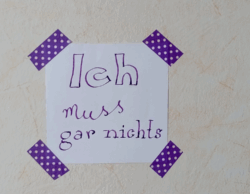 Photo von einem Notizzettel, der zur Erinnerung an meine Selbstbestimmung mit lila Klebeband an die Wand geklebt wurde. Auf dem Zettel steht: Ich muss gar nichts.