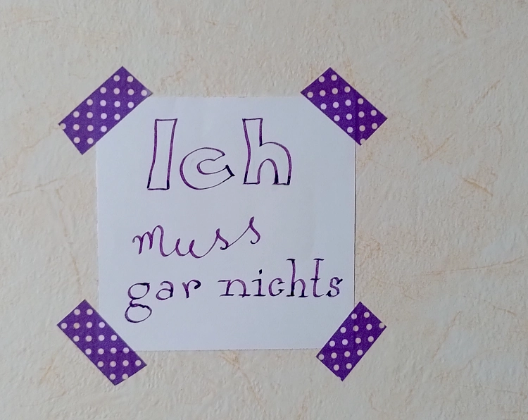Photo von einem Notizzettel, der zur Erinnerung an meine Selbstbestimmung mit lila Klebeband an die Wand geklebt wurde. Auf dem Zettel steht: Ich muss gar nichts.
