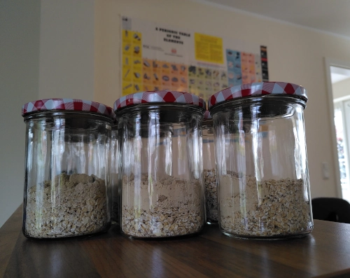 Drei verschlossene Schraubgläser mit Haferflocken und Proteinpulver darin.