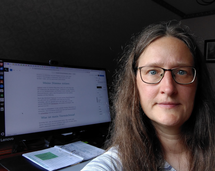 Selfie von einer Frau mit Brille vor einem Computer. Auf dem Bildschirm ist eine Blogsoftware geöffnet