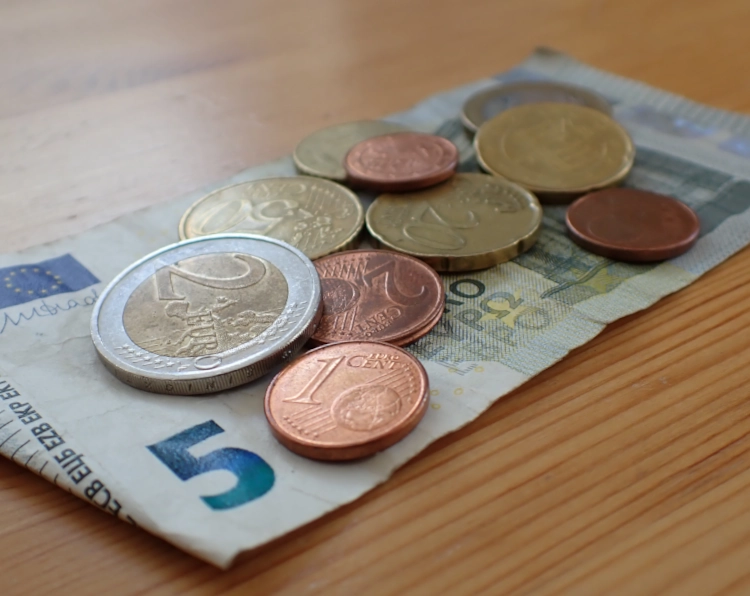 Nahaufnahme eines Fünfeuroscheins mit etwas Münzgeld darauf als Symbolbild für Bürgergeld