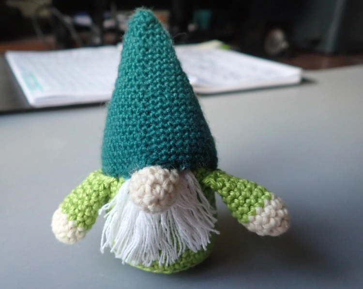 Eine grüne Figur nach meiner Häkelanleitung für Weihnachtswichtel, Er trägt eine große Mütze, aus der vom Gesicht nur noch Nase und Bart herausgucken.