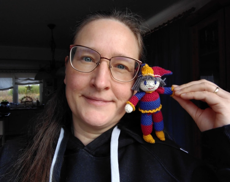 Selfie einer Frau mit einer Häkelfigur in Form eines bunten Narren auf der Schulter.