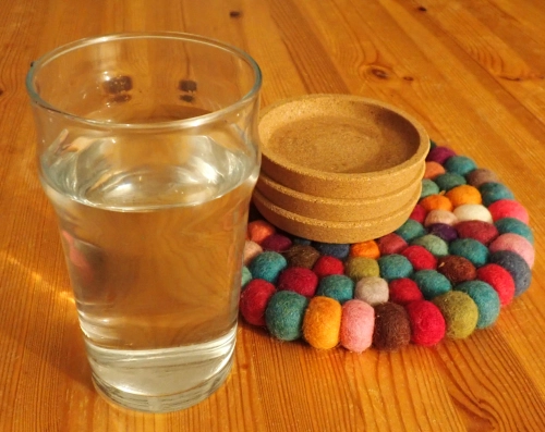 Ein Glas mit Wasser und ein Stapel Korkuntersetzer auf einer hellen Holztischplatte.
