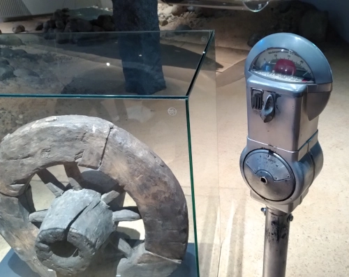 Eine Parkuhr aus dem zwanzigsten Jahrhundert neben einem antiken Holzrad.