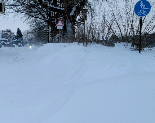Photo von einer Straße. Der Fußweg an der Seite ist mit tteils über kniehohen Schneewehen bedeckt