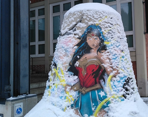 Ein glockenförmiger Poller aus Beton, darauf eine Zeichnung von Wonderwoman und Schneebelag