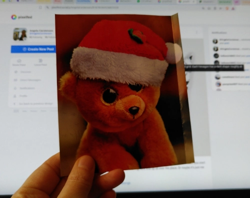 Eine Hand hält eine Weihnachtskarte, sodass die Vorderseite zu sehen ist, das Motiv ist ein Plüschbär mit einer Weihnachtsmannmütze.