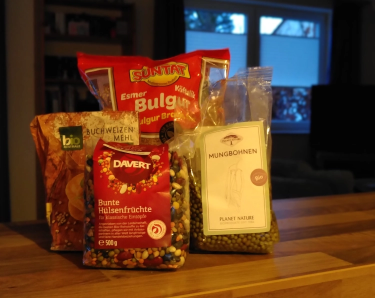 Vier Tüten auf einer Tischplatte, darin Mungbohnen, Bulgur, gemischte Hülsenfrüchte und Buchweizenmehl., als Symbolbild dafür, dass sich Vorräte sinnvoll verbrauchen lassen