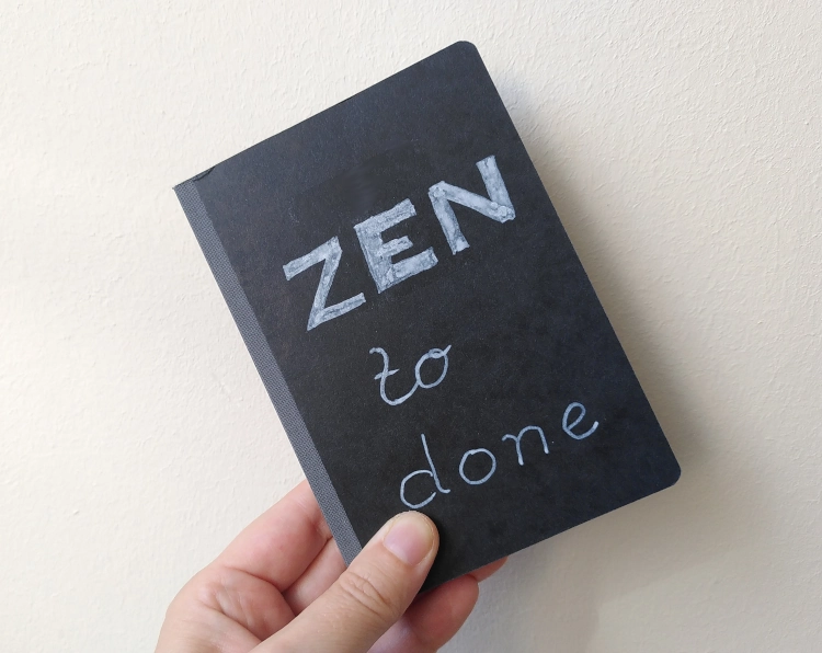 Ein kleines Notizbuch mit schwarzem Pappdeckel. Darauf in weiß geschrieben: Zen to done.