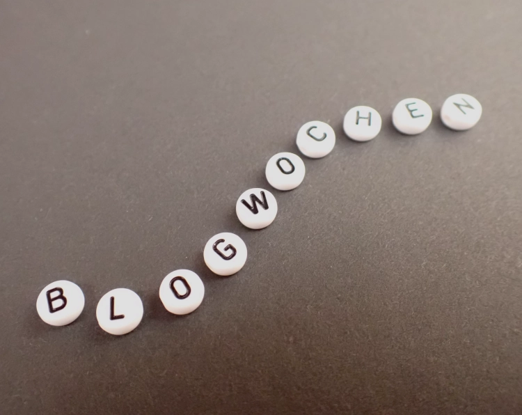 Buchstabenperlen auf einem schwazen Karton ergeben das Wort Blogwochen